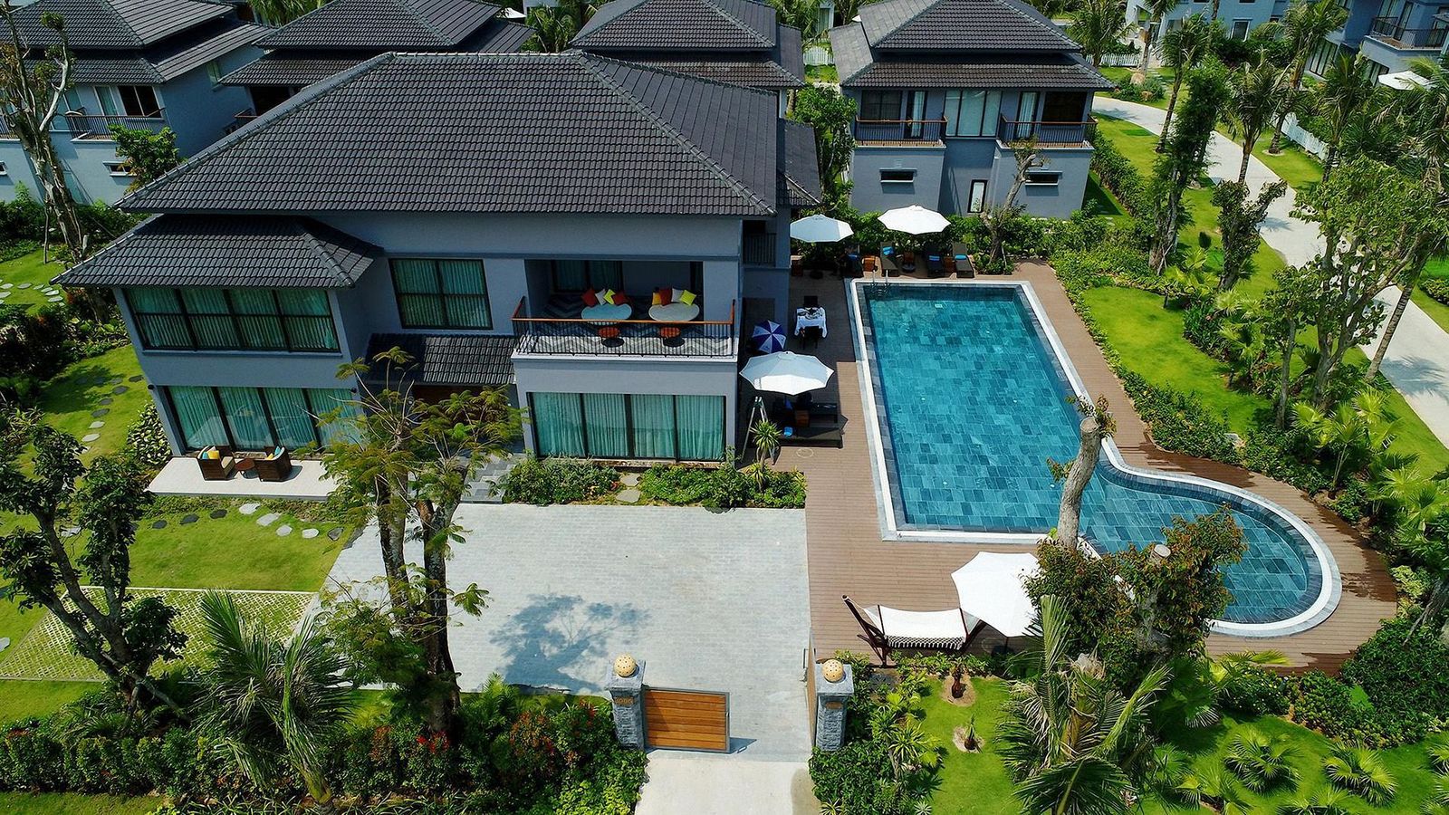 Aerial view of a dark-roofed villa with a pool set in mature gardens